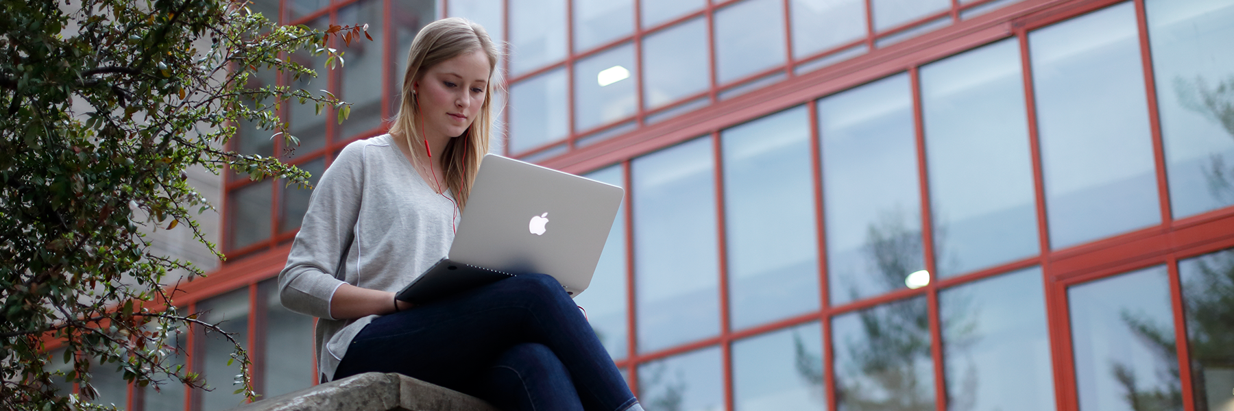 A student works on her laptop outside a campus building