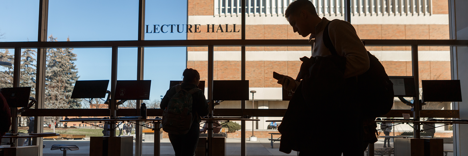 A man on a phone walks through the Lecture Hall building